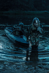 Covert landing. Pair of armed operators with painted faces disembarking river coast from military...