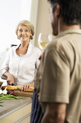 Senior woman cutting baguette, man drinking a glass of white wine