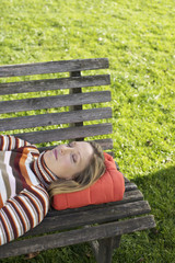 Young woman lying dozing on a wooden bench, high angle view