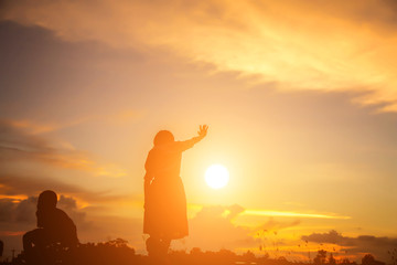 a silhouette of a happy young girl child the arms of his loving mother for a hug, in front of the sunset in the sky on a summer day.