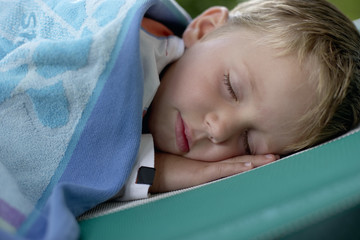 Little boy wrapped in a cover lying on a beach chair, close-up