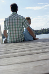 Fototapeta premium Father and son sitting on a wooden footbridge next to each other, selective focus