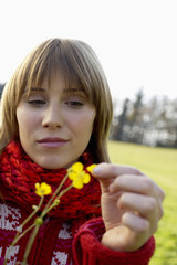 Young woman with scarf and cardigan holding flowers in her hand, close-up