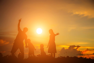 a silhouette of a happy young girl child the arms of his loving mother for a hug, in front of the sunset in the sky on a summer day. 