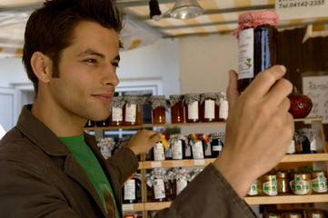Young man with black hair examining a preserving glass with jam, selective focus
