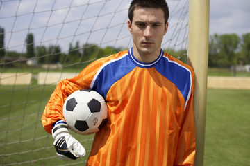 Goalkeeper holding ball leaning against goal, portrait