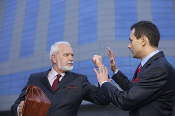 Mature businessman with fist up, an other businessman holding hands up