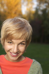 Blonde girl with a toothy smile in a park, close-up, selective focus