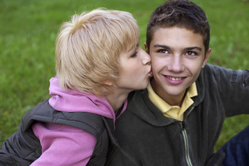 Teenage girl kissing a teenage boy on the cheek, close-up, selective focus