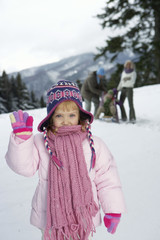 Girl waving at camera, family in background