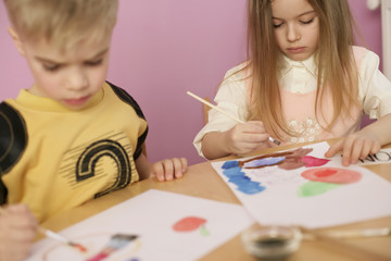 Two children sitting at a table, painting with watercolors