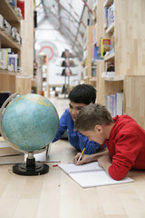 Two boys lying on a floor next to a globe and making notes, fully_released