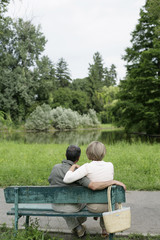 Fototapeta premium Mature couple sitting on a bench, looking at a small lake