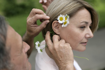 Mature man putting flowers behind woman's ear