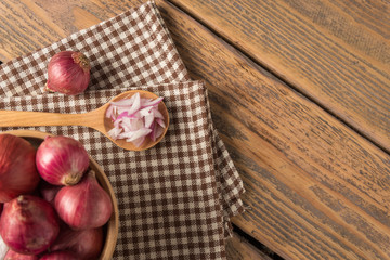Sliced onion in spoon and red onion in bowl on wood table.