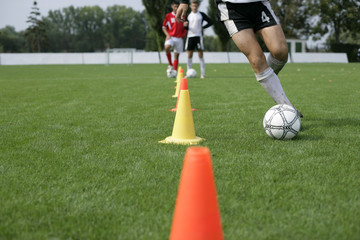 Fototapeta premium Soccer player running with football slalom around pylons