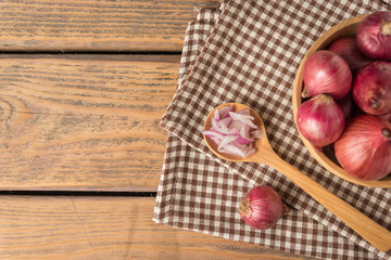 Sliced onion in spoon and red onion in bowl on wood table.