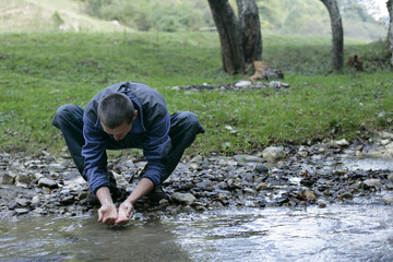 Brunette man is washing his hands at the shore of a rivulet