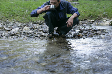 Young man is drinking water from a rivulet (part of)