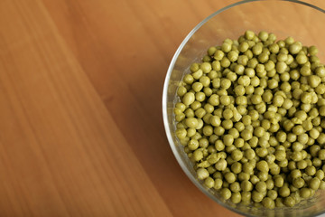 Glassy bowl with peas on a wooden underlay, high angle view