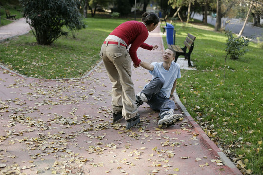 Young girl with inline skates helping boy to stand up