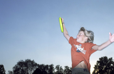 Blonde Boy catching a Frisbee while jumping into the Air - Game - Leisure Time - Youth - Park -...