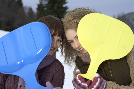 Two young women holding plastic slide-shovels in their gloved hands, portrait