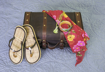 Vintage suitcase with sandals, bracelet, scarf and necklace draped on it, tropic travel concept