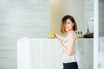 Wellness, healthcare, lifestyle. Young gorgeos smilling woman with short brown hair waiting in front of reception in beauty or spe salon.