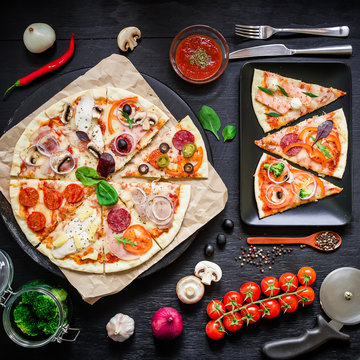 Tasty pizza with ingredients, spices and cutlery on black background. Flat lay, top view.