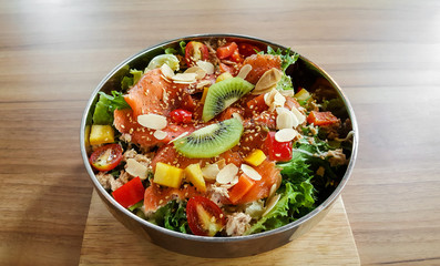 Bowl smoked salmon fruit salad on natural wood table.