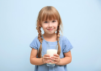 Portrait of little girl with glass of milk on blue background