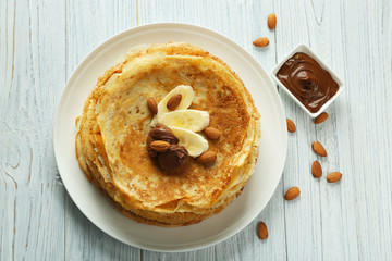 Delicious pancakes with banana and chocolate on white wooden background
