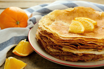 Stack of delicious pancakes with orange on wooden table