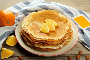 Stack of delicious pancakes with orange on wooden table