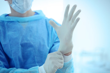 Young doctor putting on rubber gloves in clinic, closeup