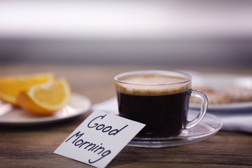 Cup of coffee, orange slices and note GOOD MORNING on kitchen table