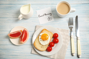 Delicious breakfast and GOOD MORNING greeting note on wooden table, top view