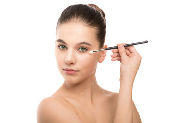 Obraz premium Portrait of beautiful young brunette woman with clean face. Beauty spa model girl with perfect fresh clean skin applying cosmetic brush. Youth and skin care concept. Isolated on a white background.