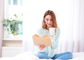 Young beautiful woman reading book and drinking tea at home