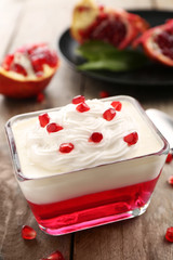 Tasty jelly dessert with pomegranate seeds and cream on wooden table