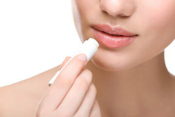 Woman applying hygienic lip balm on white background - obrazy, fototapety, plakaty