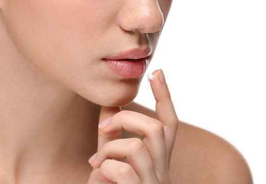 Woman applying cream onto lips on white background