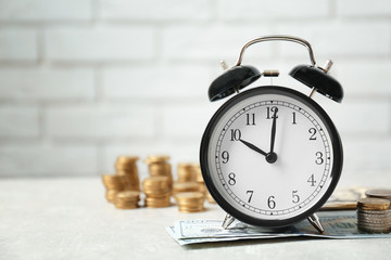 Alarm clock and money on white table against brick wall background