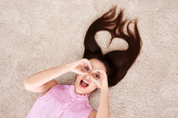 Beautiful young woman with heart-shaped hair strands lying on carpet at home