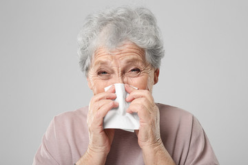 Portrait of elderly woman sneezing in handkerchief on grey background