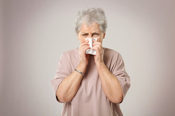 Portrait of elderly woman sneezing in handkerchief on grey background