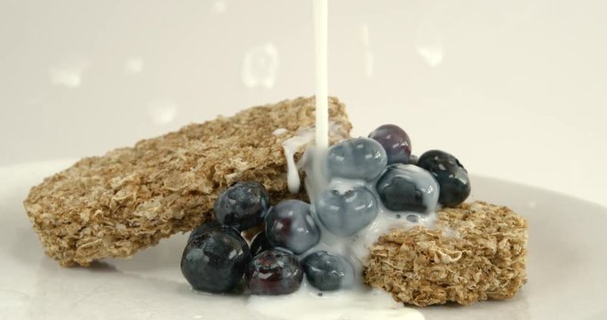 Pouring milk on breakfast cereal with blueberry fruit