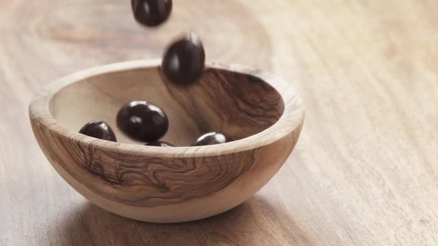 Slow motion of almonds covered with chocolate fall in wood bowl on wooden table, 180fps prores footage