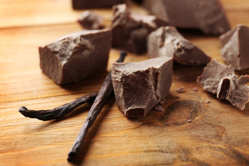 Broken chocolate pieces with vanilla sticks on wooden background